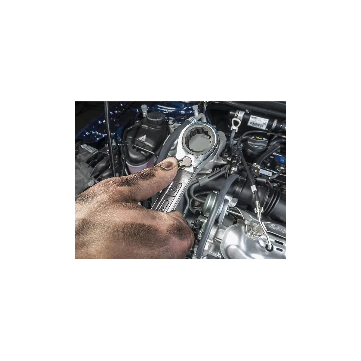 Schmutzige Hand hält einen Schraubenschlüssel in einem Motorraum.