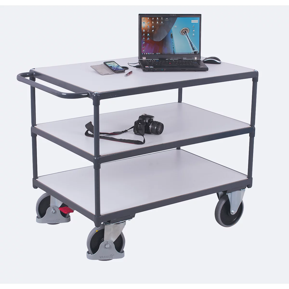A three-tiered serving cart with laptop, camera, and accessories. Gray frame, white shelves, wheels.