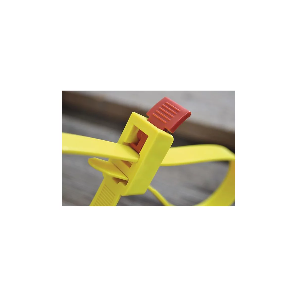 Collier de serrage jaune avec fermoir rouge. Le collier est partiellement fermé et repose sur une surface en bois.