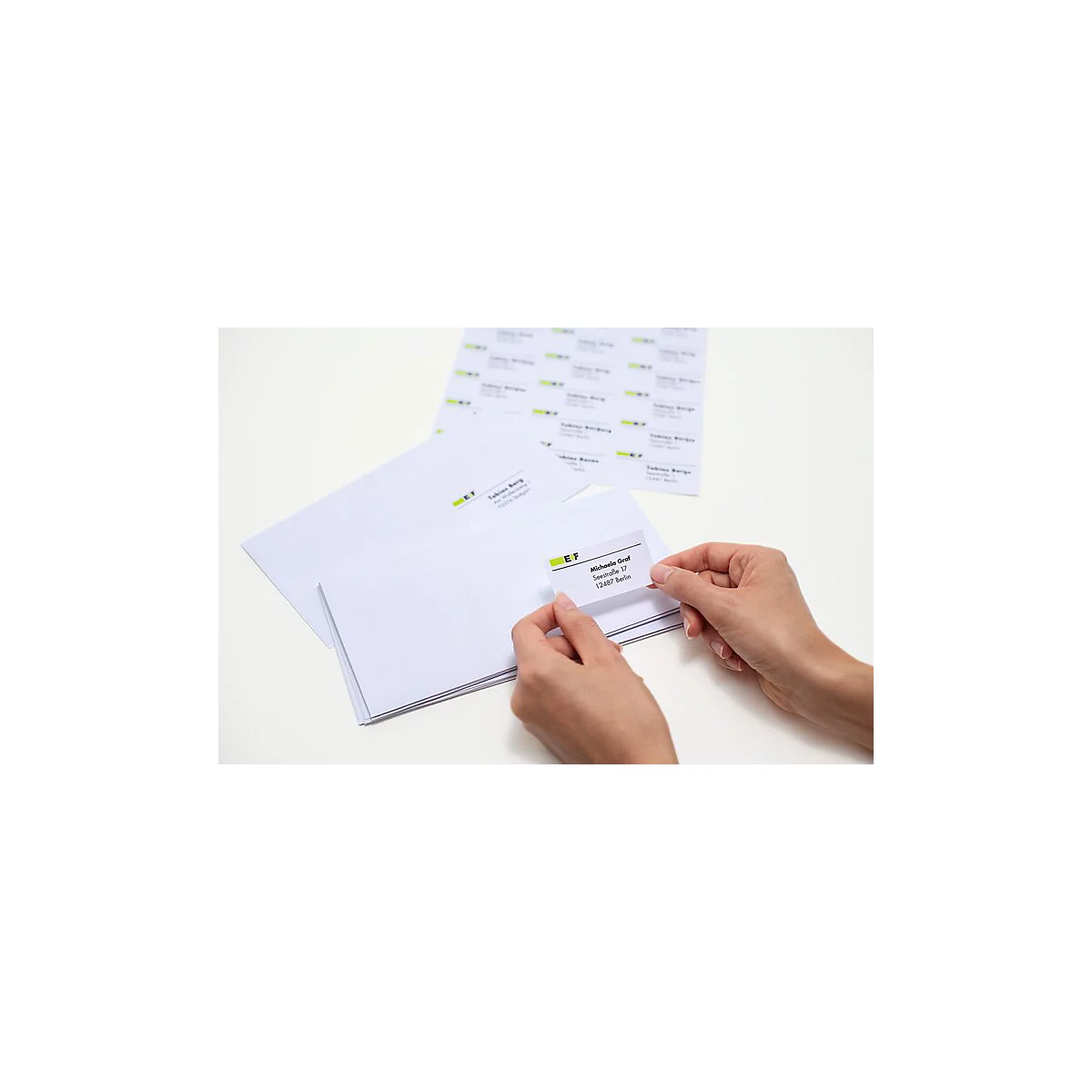 Handen houden een adreslabel boven een envelop. Op de achtergrond zijn meer enveloppen en stickers te zien.