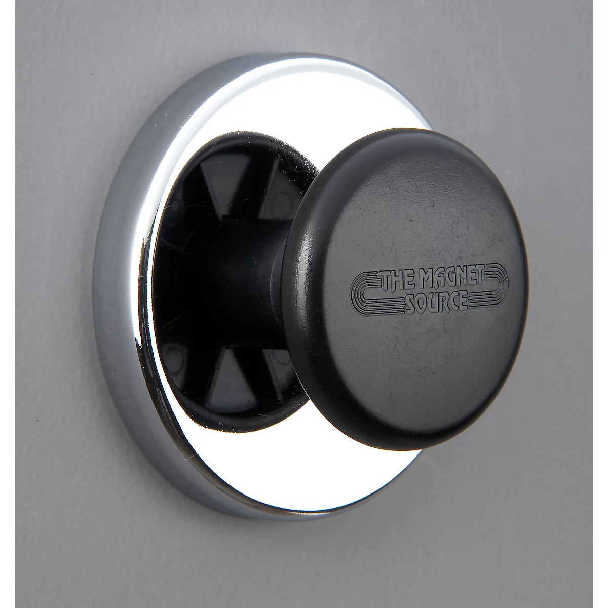 Black magnet with "THE MAGNET SOURCE" on a silver ring on a grey wall.