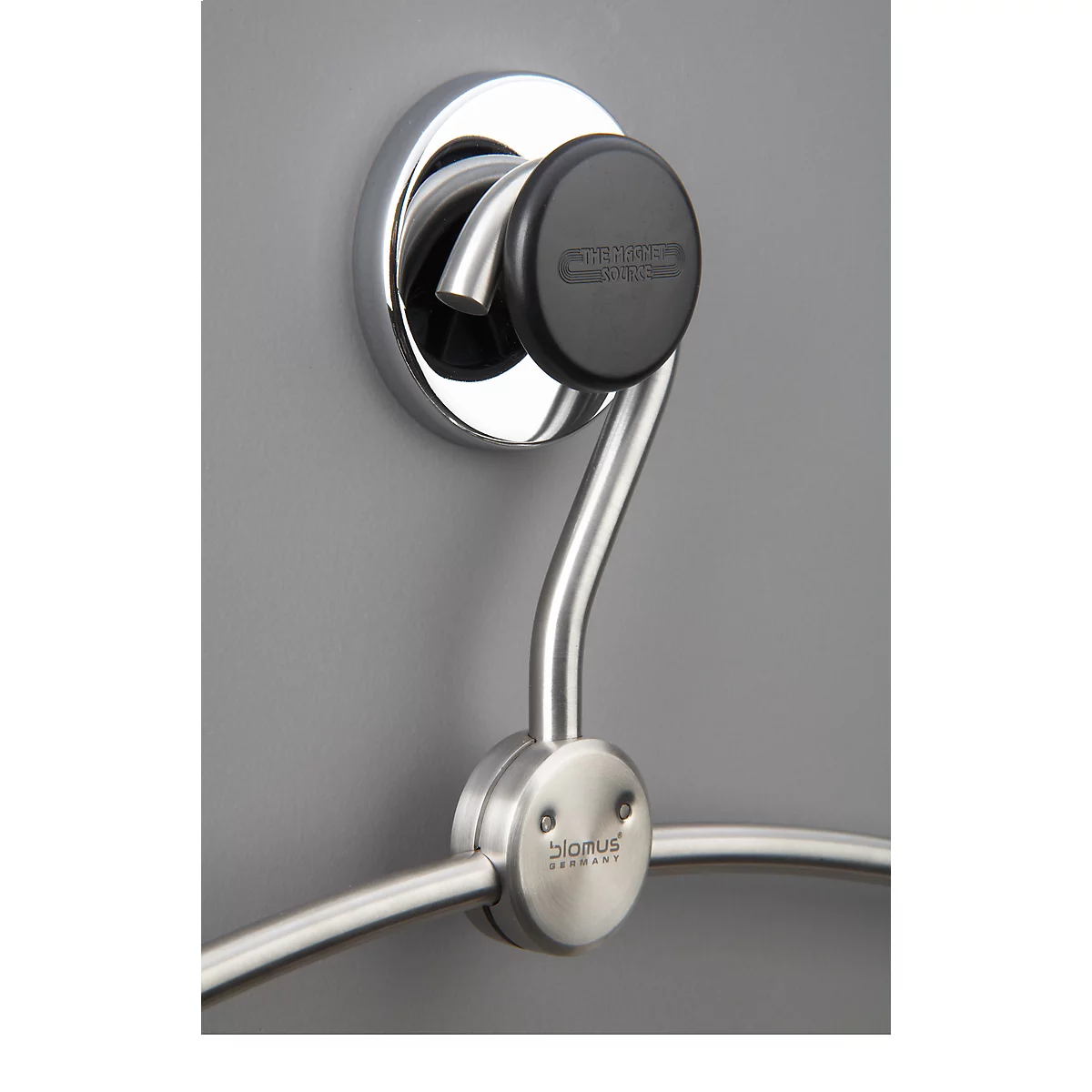 Chrome towel holder, mounted on grey wall. Black knob with lettering. Below the bracket a towel ring.