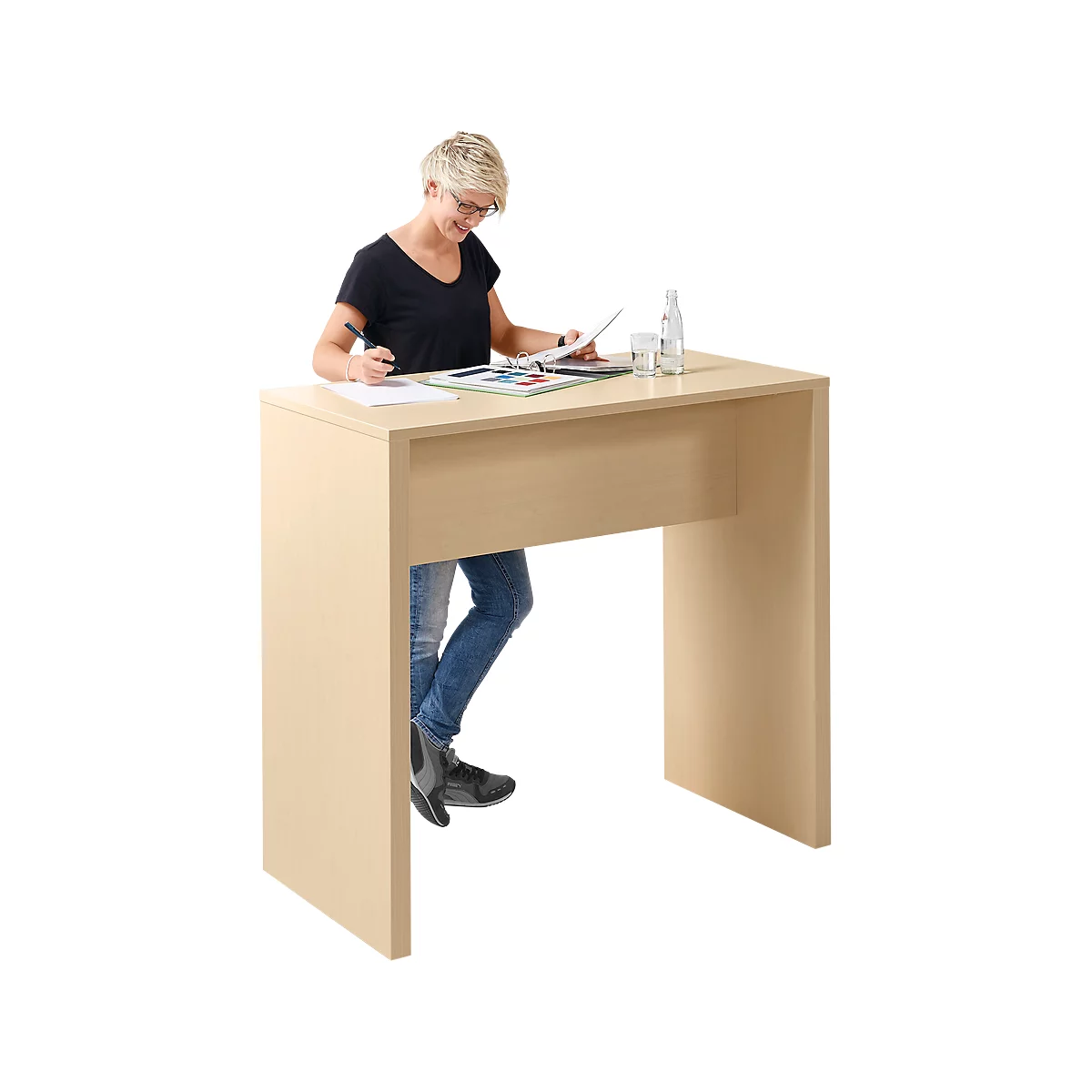Woman standing at a light-colored desk, wearing glasses, a black shirt, and jeans.