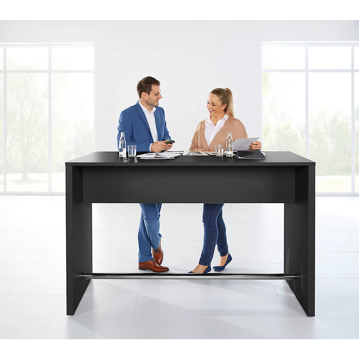Mann und Frau stehen an einer schwarzen Stehtisch-Theke, sprechen sich an, helles Büro im Hintergrund.