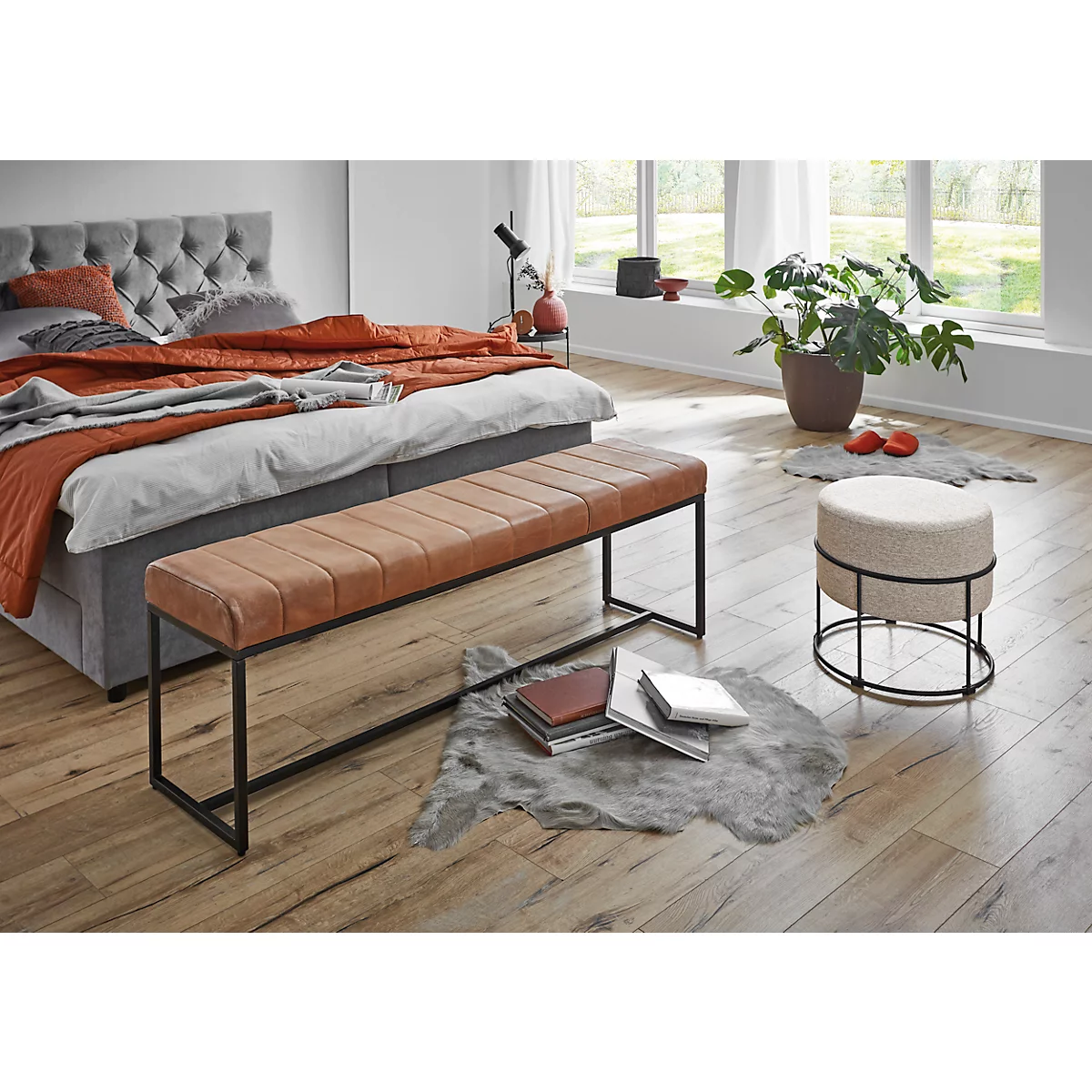 Schlafzimmer mit Bett, brauner Bank, Hocker und Pflanzen.