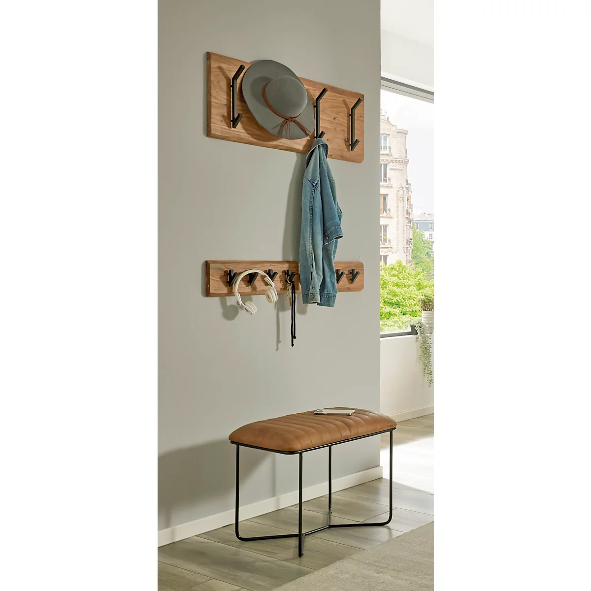 Hölzerne Wandgarderobe mit Hut und Jacke. Darunter weitere Haken mit Kopfhörern. Darunter eine braune Sitzbank.