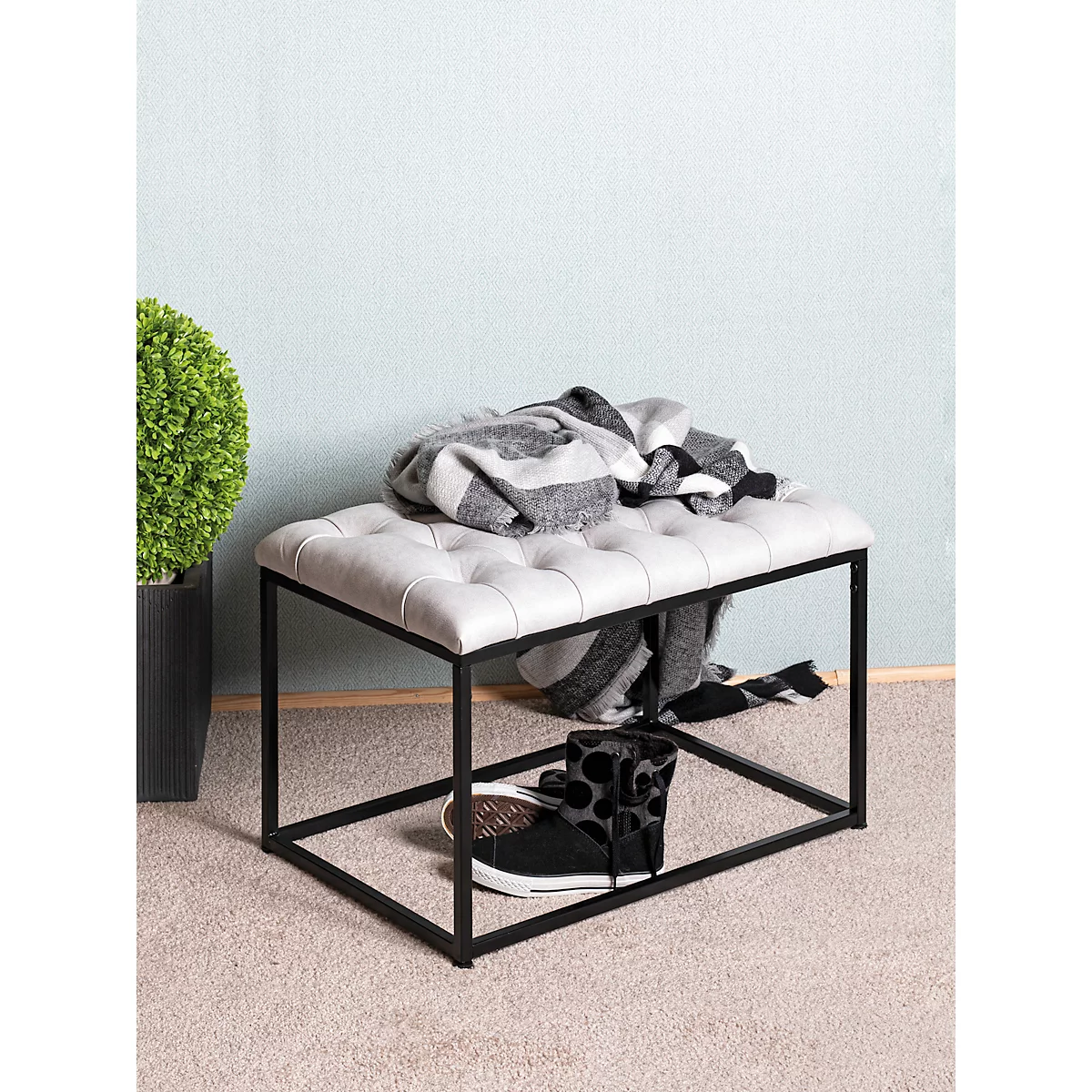 Quadratischer, gepolsterter Hocker mit grauer, gesteppter Sitzfläche und schwarzem Metallgestell.