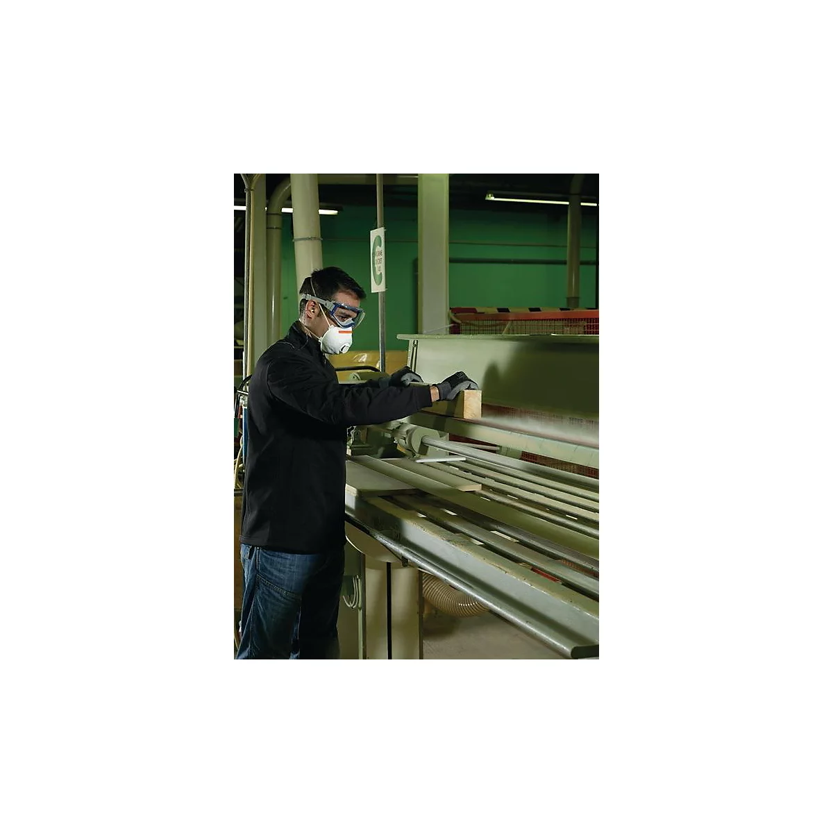 Een man met een veiligheidsbril en een masker bewerkt hout op een machine in een werkplaats.