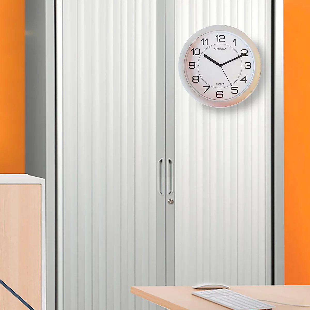 Horloge avec aiguilles noires sur un mur d'armoire blanc. Un clavier et une souris sont sur la table.