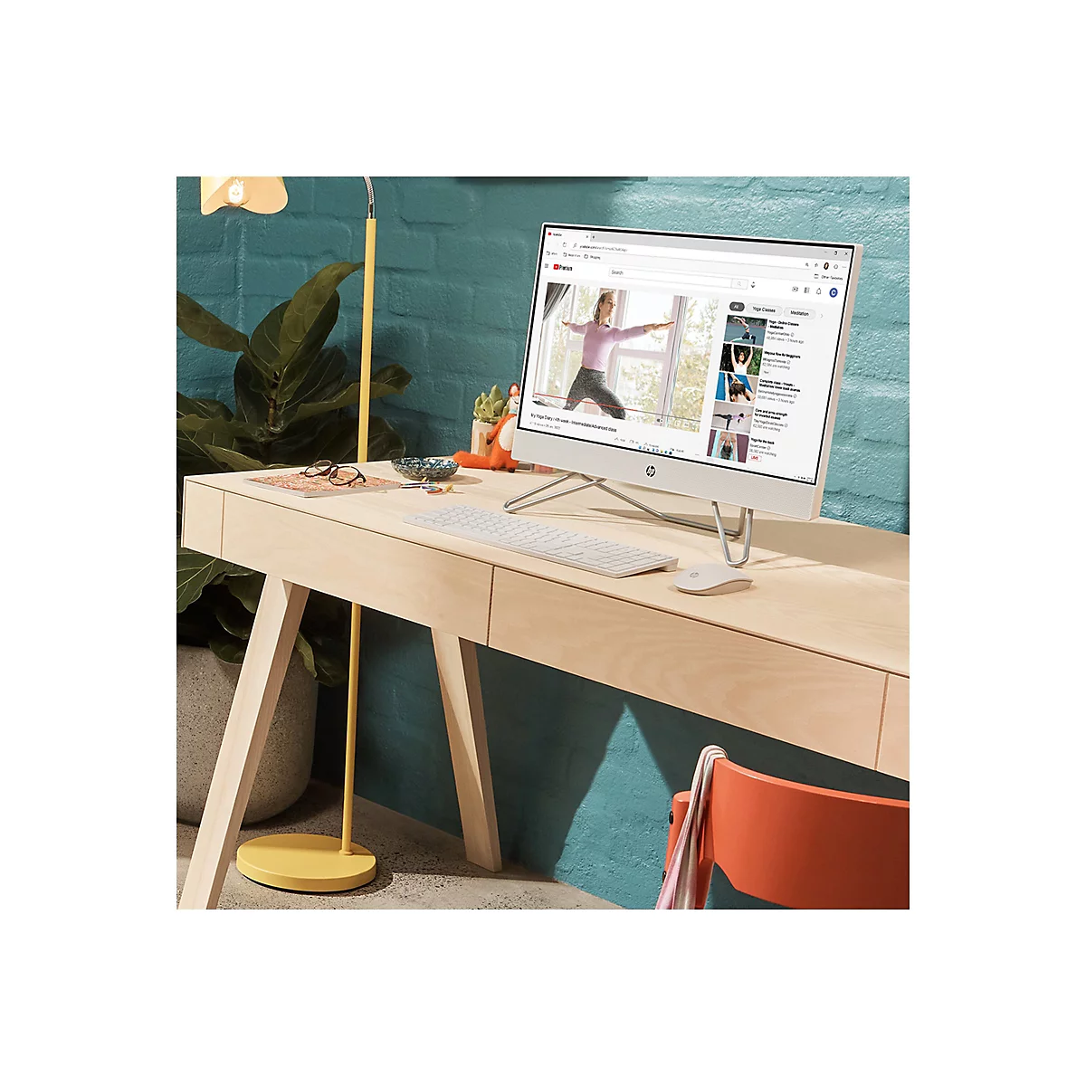 Ein weißer HP-All-in-One-PC steht auf einem Holzschreibtisch. Auf dem Bildschirm läuft ein Yoga-Video. Auf dem Tisch liegen eine Tastatur, eine Maus, eine Brille und Dekoration.