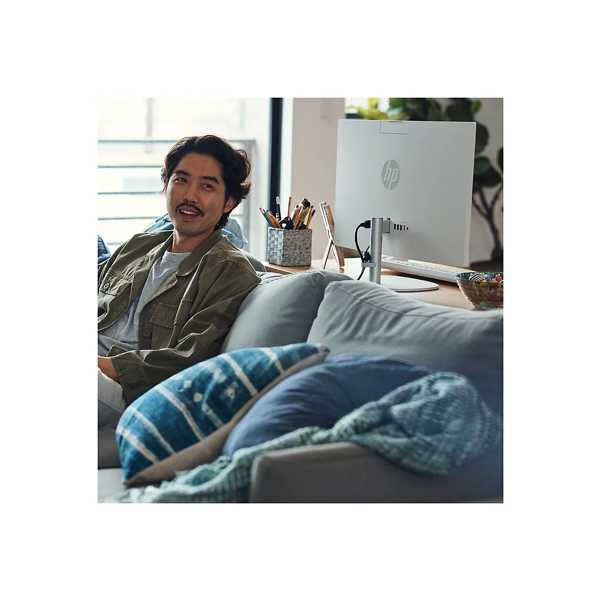 Ein Mann sitzt auf einem Sofa und lächelt in die Kamera. Hinter ihm steht ein weißer HP-Monitor auf einem Tisch.