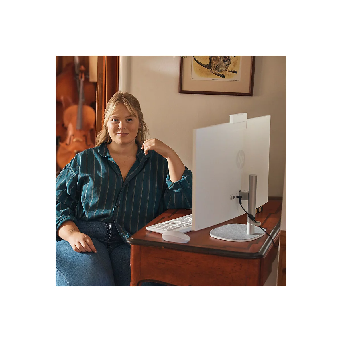 Eine Frau sitzt an einem Schreibtisch vor einem weißen Computer. Sie lächelt in die Kamera. Auf dem Tisch befinden sich eine Tastatur und eine Maus.