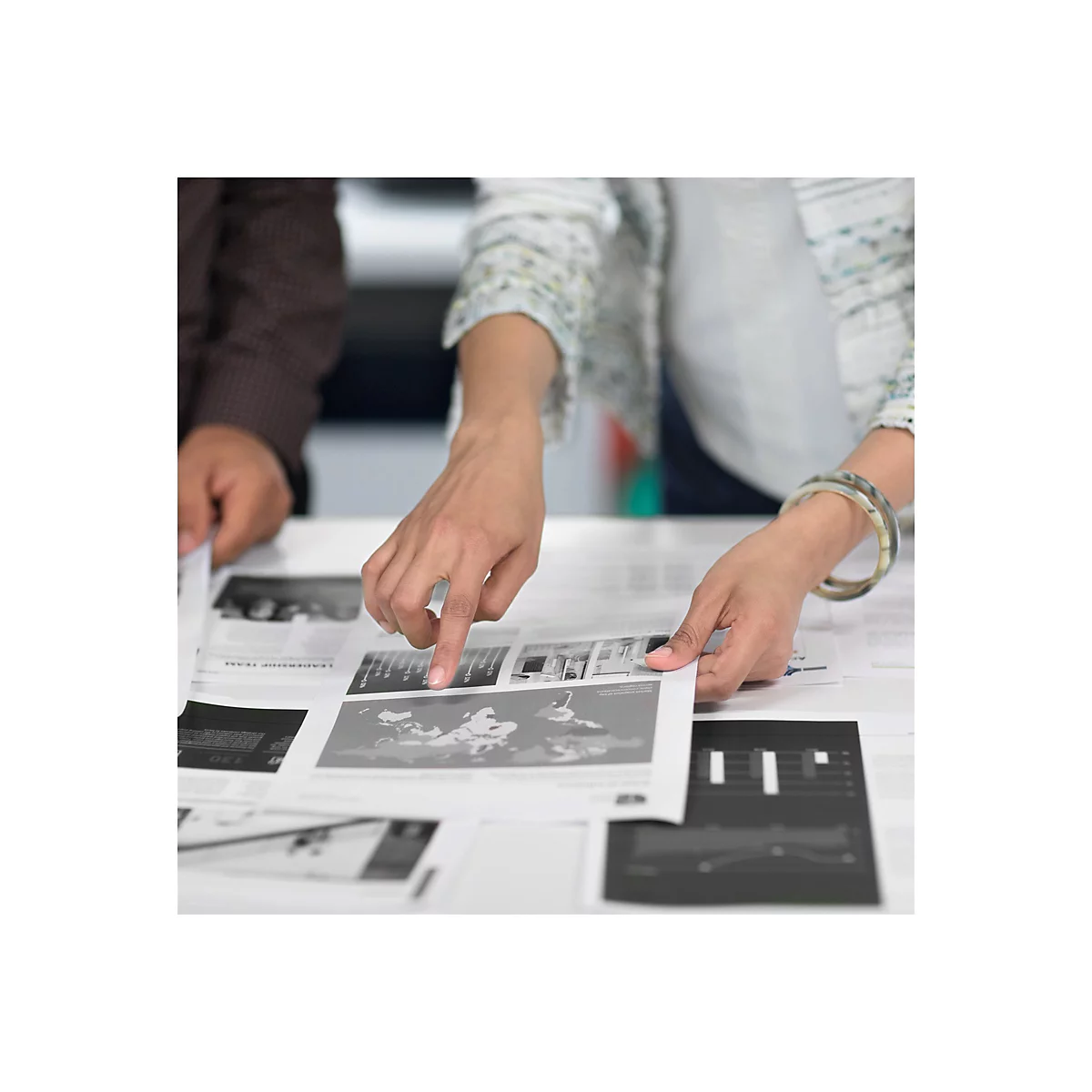 Deux personnes examinent ensemble des impressions avec des graphiques et des cartes. Une main pointe vers une image.