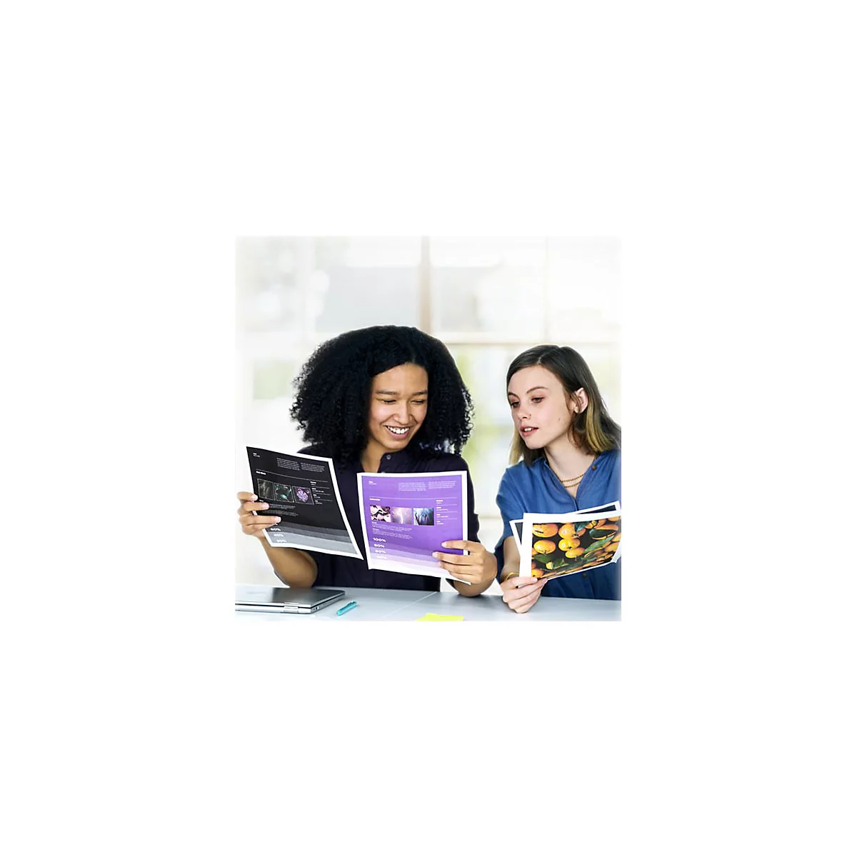 Zwei Frauen betrachten Unterlagen. Eine Frau lächelt und zeigt auf ein Dokument. Die andere Frau betrachtet ein Bild von Orangen.