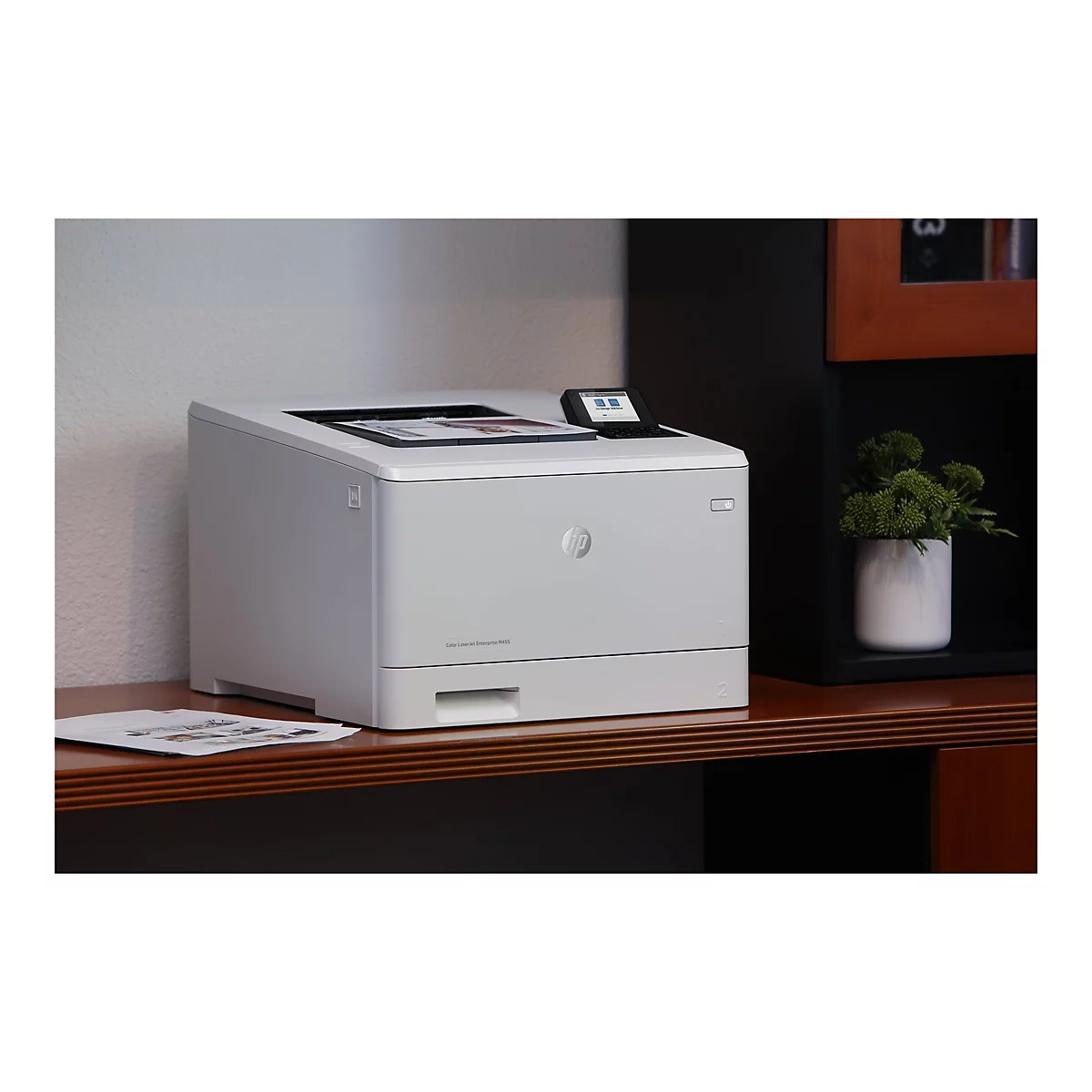 Grauer Drucker auf braunem Schreibtisch. Kleines Display und HP-Logo. Auf dem Tisch liegen Blätter und eine grüne Pflanze.