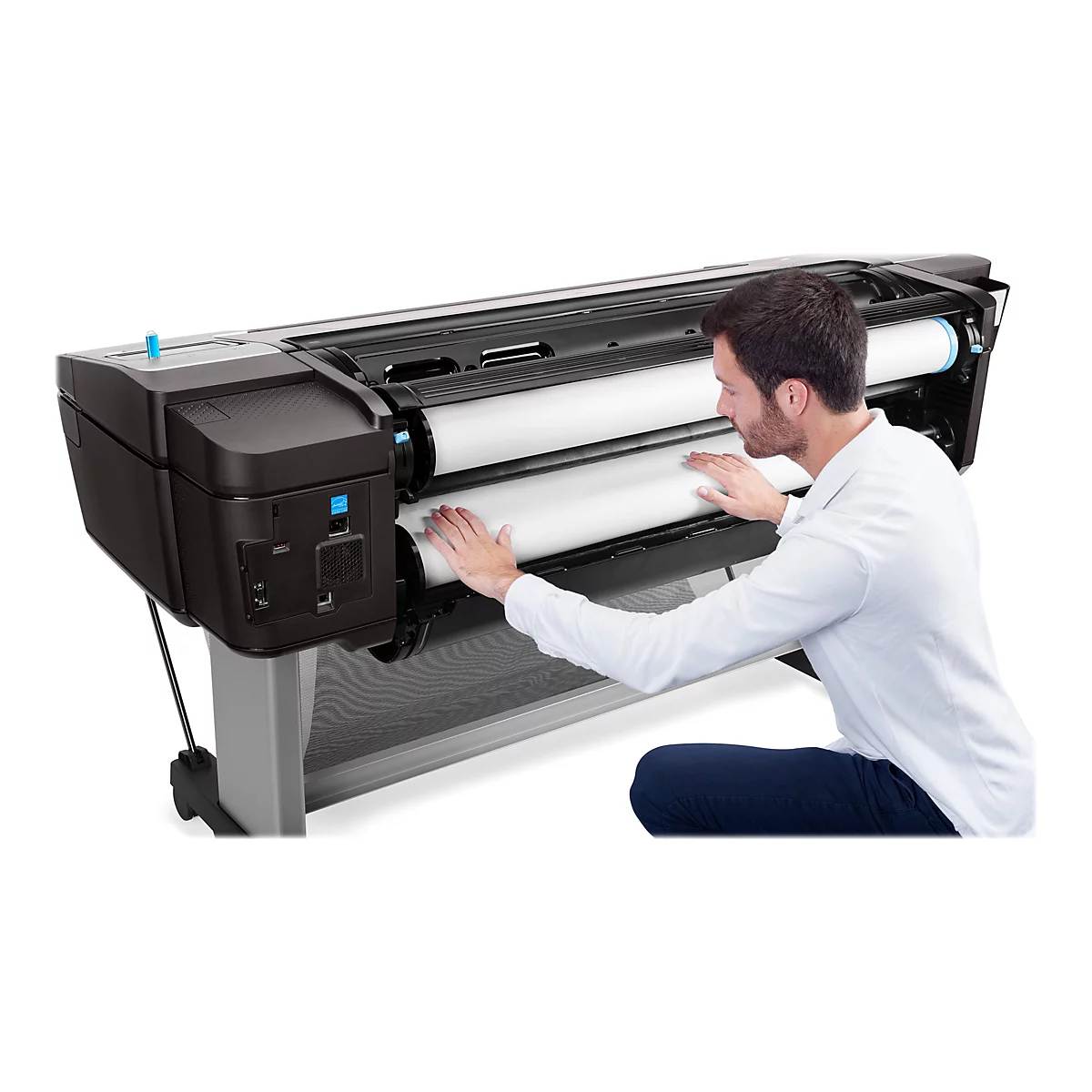 Ein Mann kniet vor einem großformatigen Drucker und legt Papier ein.