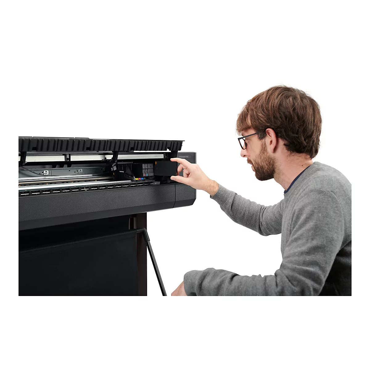 Ein Mann mit Brille setzt eine Tintenpatrone in einen Großformatdrucker ein. Er blickt konzentriert auf die Arbeit.