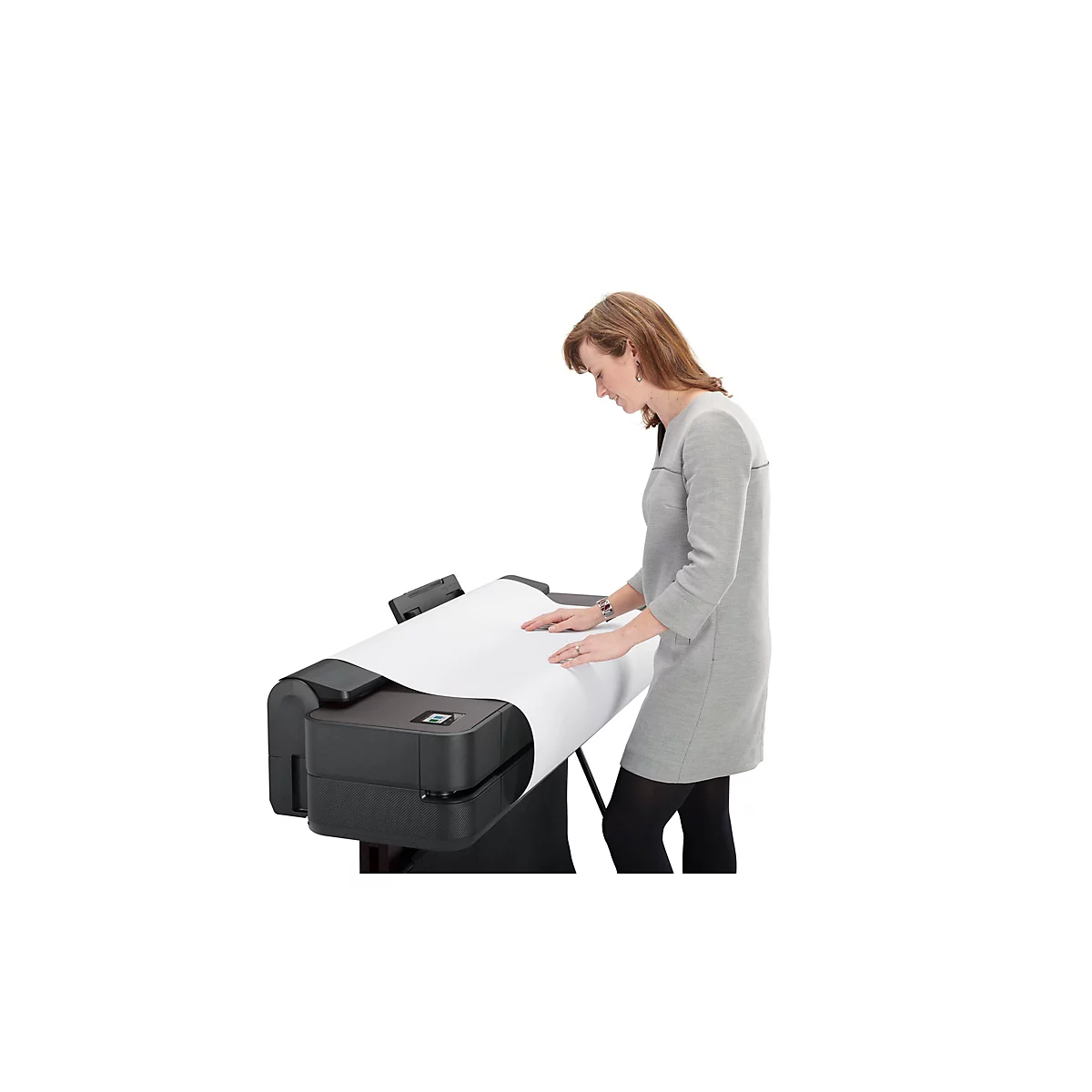 Une femme en robe grise travaille sur une imprimante grand format ; elle examine le papier imprimé.