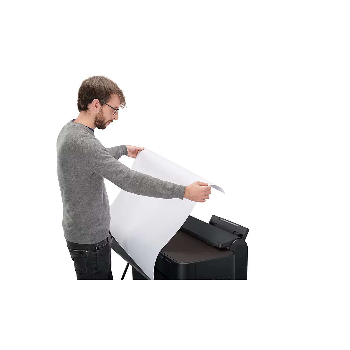 Ein Mann mit Brille hält ein großes weißes Blatt Papier in der Hand, neben einem schwarzen Drucker.