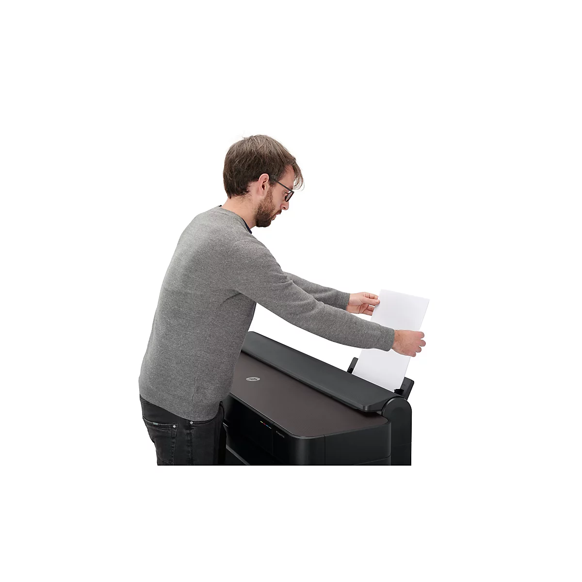 Ein Mann mit Brille legt Papier in einen schwarzen Drucker. Er trägt ein graues Sweatshirt und Jeans.