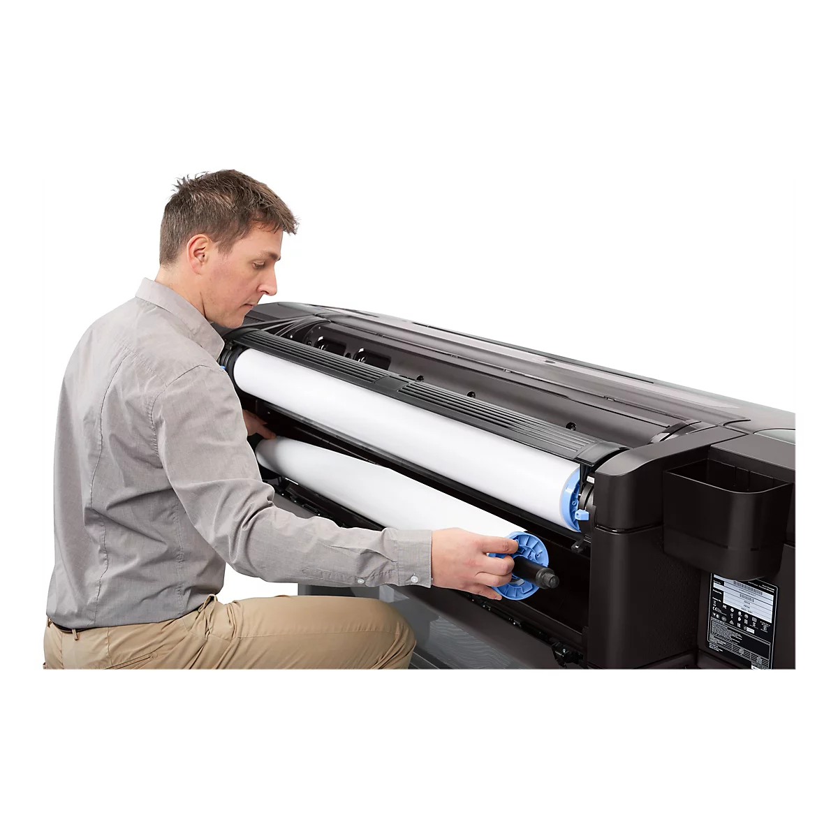 Ein Mann wechselt eine Papierrolle in einem GroÃŸformatdrucker. Er kniet und hÃ¤lt die neue Rolle.