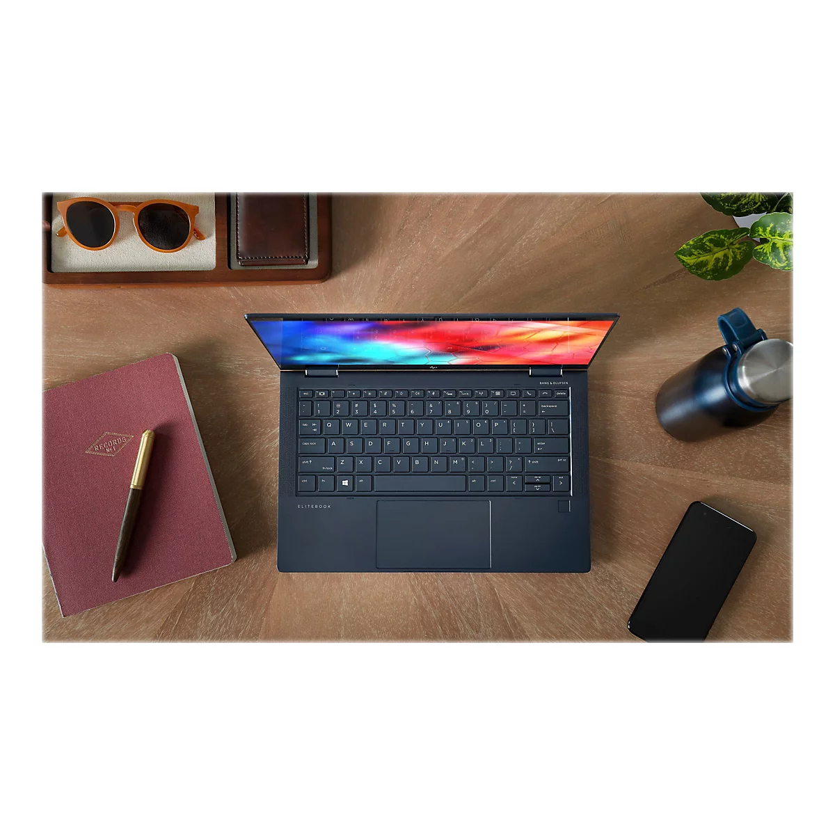 Dunkelblauer Laptop auf HolzoberflÃ¤che, daneben Sonnenbrille, Notizbuch, Stift, Trinkflasche und Handy.