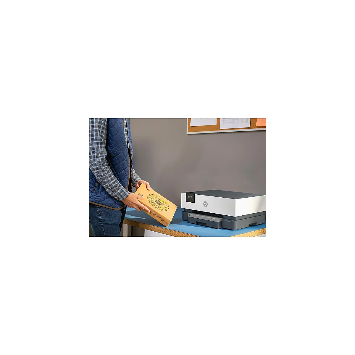 Une personne tenant une boîte à pizza à côté d'une imprimante HP. Une note est posée sur la table. Nappe bleue.