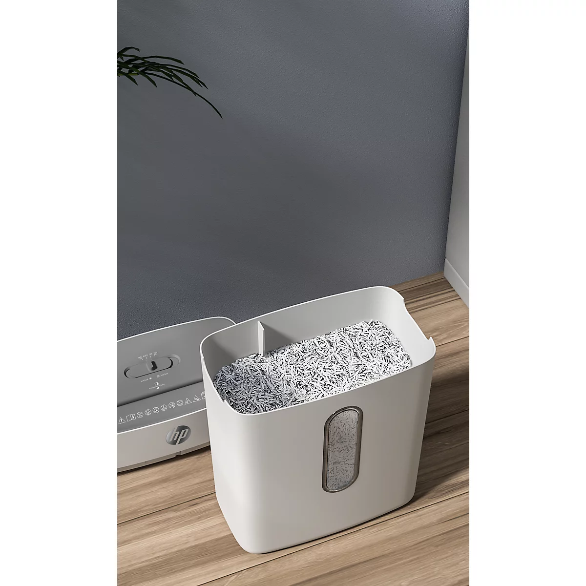 White paper shredder filled with shredded paper, on a wooden floor.