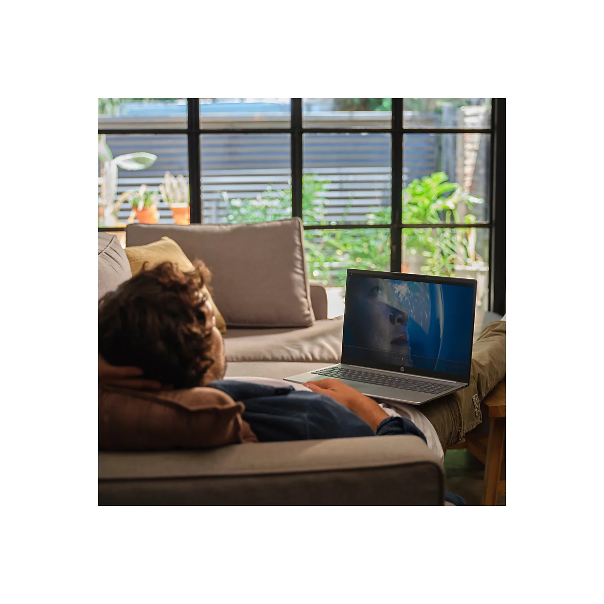 Ein Mann liegt auf einem Sofa und schaut auf einem Laptop einen Film. Das Laptop zeigt eine Frau in einem Astronautenhelm.