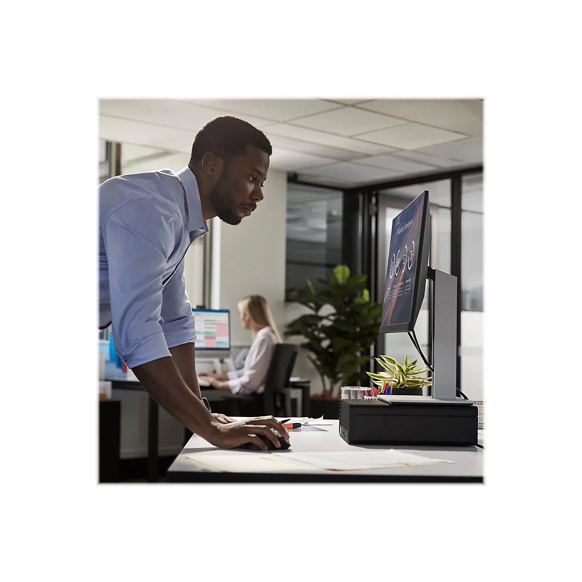 Ein Mann im BÃ¼ro, der auf einen Monitor blickt. Im Hintergrund arbeitet eine weitere Person.