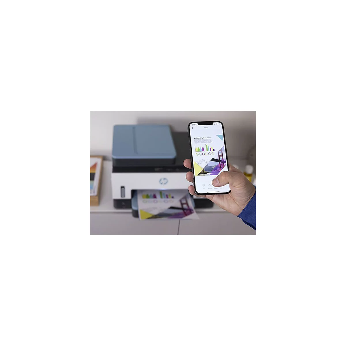 Person, die ein Smartphone hält, das eine Vorschau zeigt. Der Drucker druckt ein Papier. Das Smartphone-Display zeigt ein farbenfrohes Diagramm.