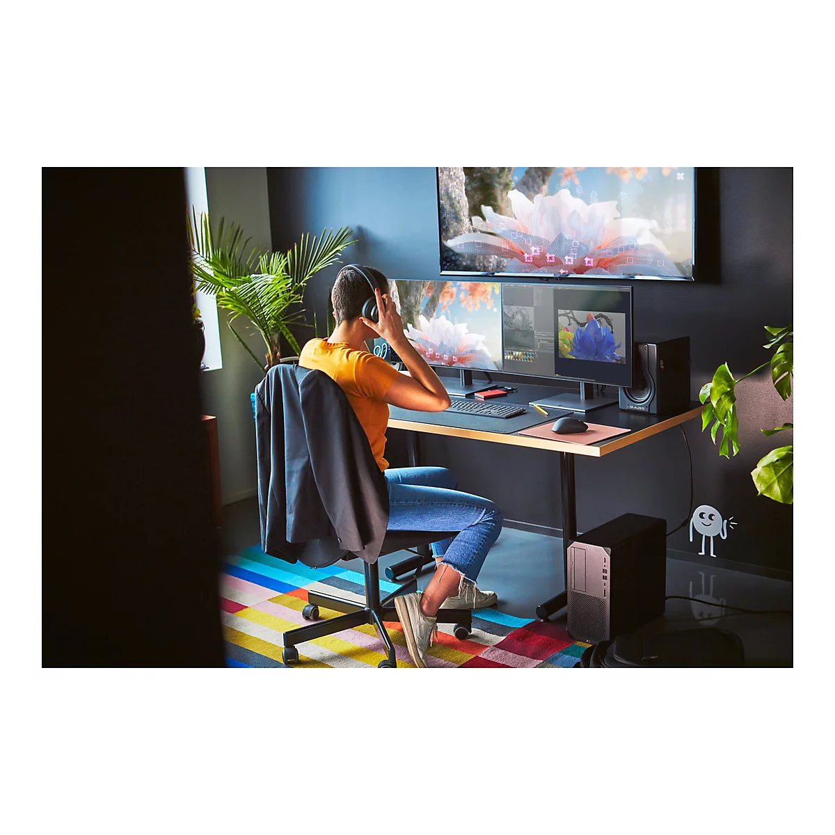 Person mit KopfhÃ¶rern sitzt vor Computerbildschirmen. Auf dem Tisch liegen Maus, Tastatur und Konsole.