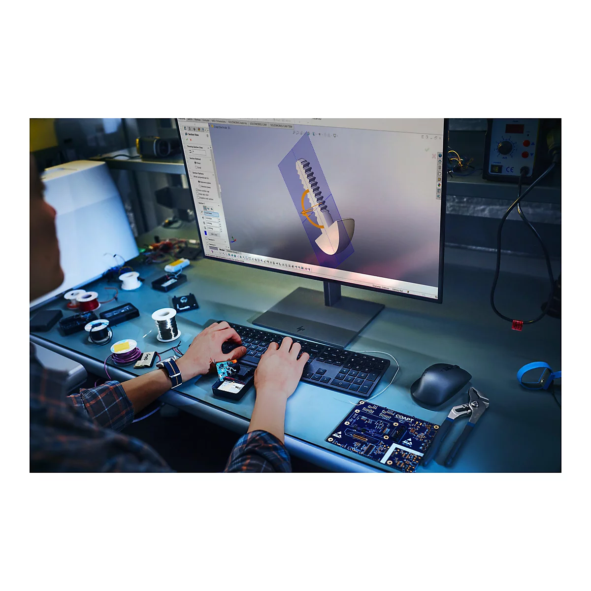 Person am PC, HÃ¤nde auf Tastatur, am Bildschirm CAD-Design eines Produkts. Werkbank mit Elektronikteilen.