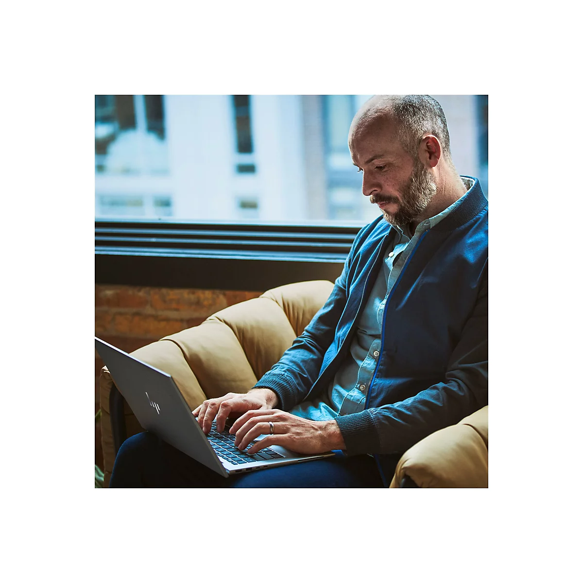 Ein Mann mit Bart sitzt in einem Sessel und arbeitet an einem Laptop.