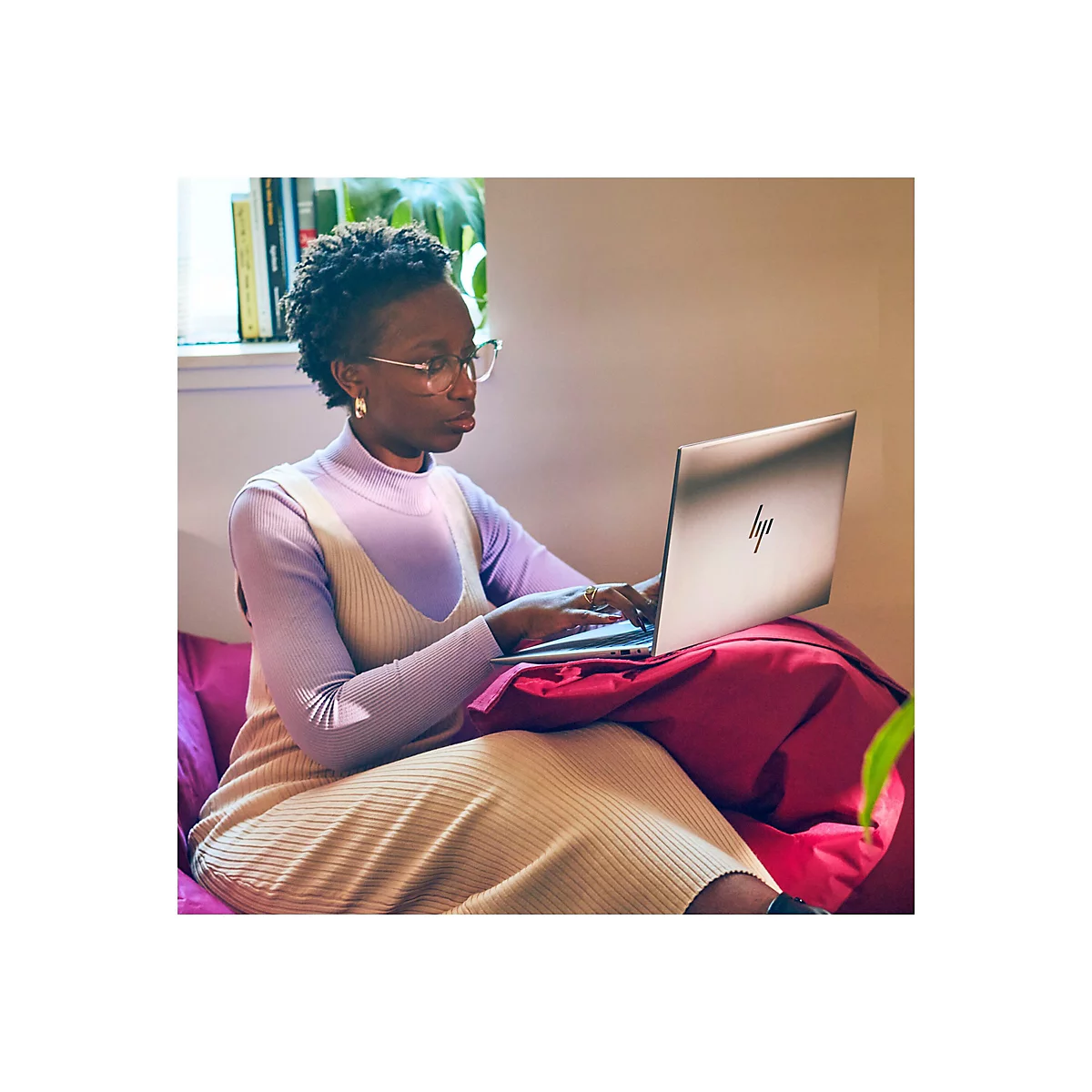 Eine Frau mit Brille sitzt auf einem Kissen und arbeitet an einem Laptop. Der Laptop hat ein HP-Logo.