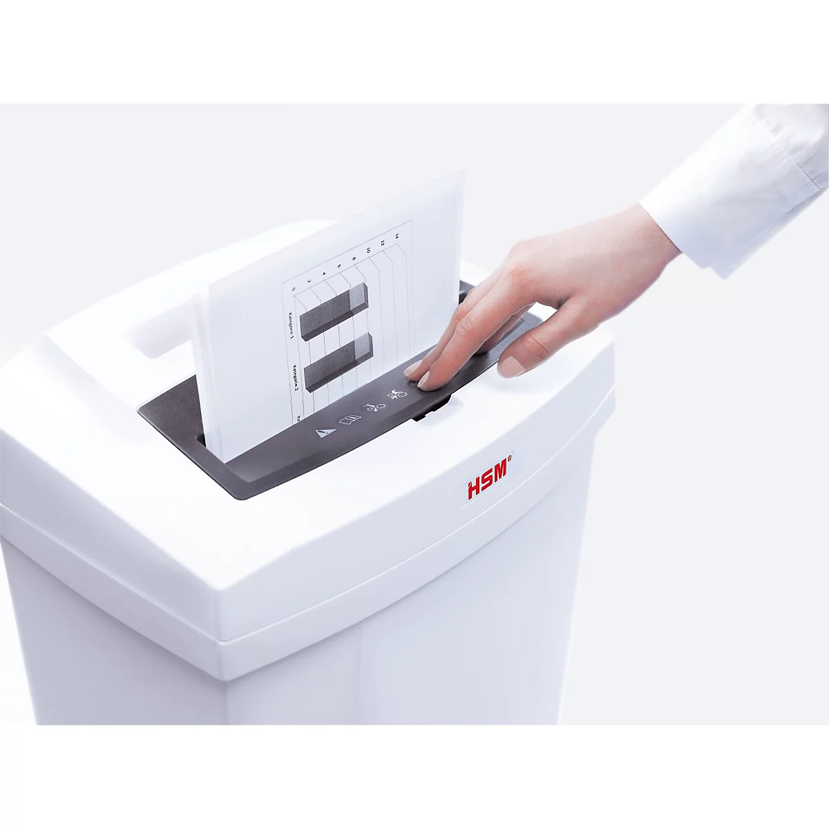 A person places paper into a shredder. The paper has lines and rectangular holes. The shredder is white with the inscription "HSM".
