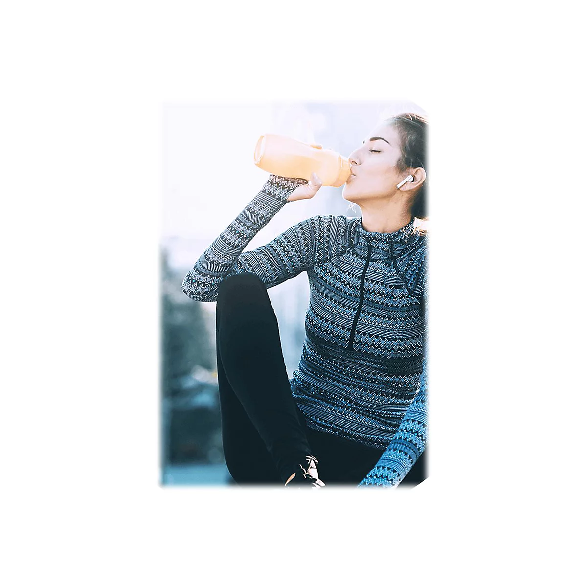 Eine Frau trinkt aus einer gelben Wasserflasche. Sie trägt Sportkleidung und Kopfhörer.