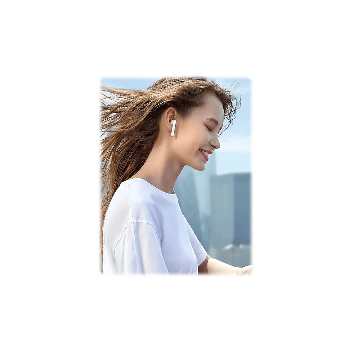 Lächelnde Frau mit Kopfhörern, die im Wind steht. Sie trägt ein weißes Shirt.