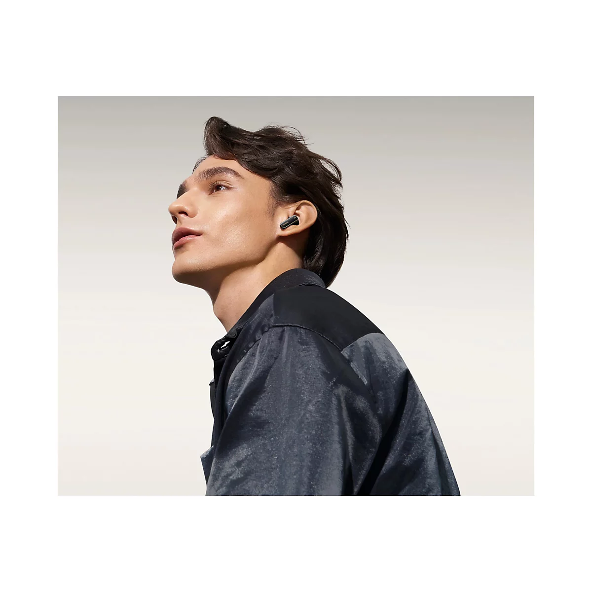 Ein Mann mit In-Ear-KopfhÃ¶rern im Ohr, der in die Ferne blickt.