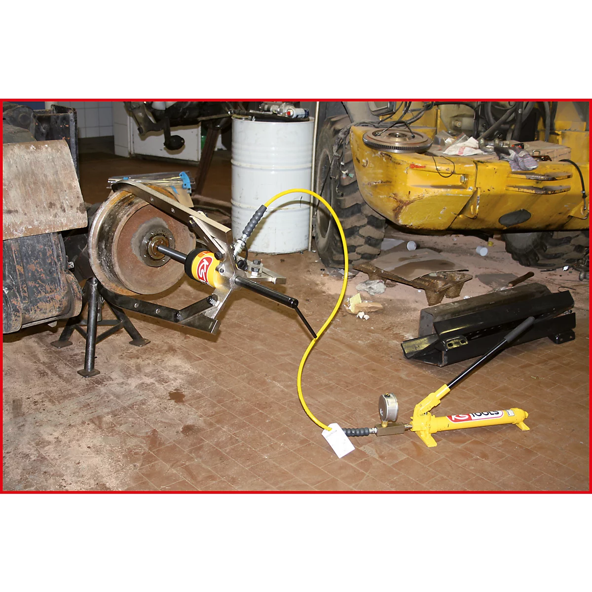 Hydraulikwerkzeug an einer Radnabe. Gelbe Kabel und Pumpe, Rost und Metall. Werkstattumgebung.