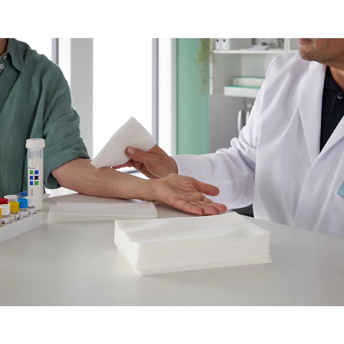 Ein Arzt tupft eine Patientenhand mit einem weißen Tuch ab.