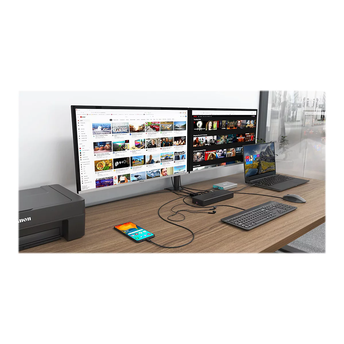 Schreibtisch mit zwei Monitoren, Laptop, Smartphone, Drucker, Maus und Tastatur. Die Bildschirme zeigen YouTube und Netflix.