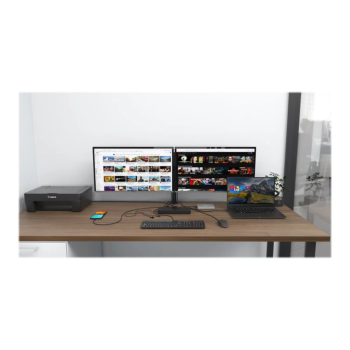 Ein Schreibtisch mit zwei Monitoren, Laptop, Drucker, Tastatur, Maus und Smartphone. Auf den Monitoren werden YouTube und Netflix Inhalte gezeigt.
