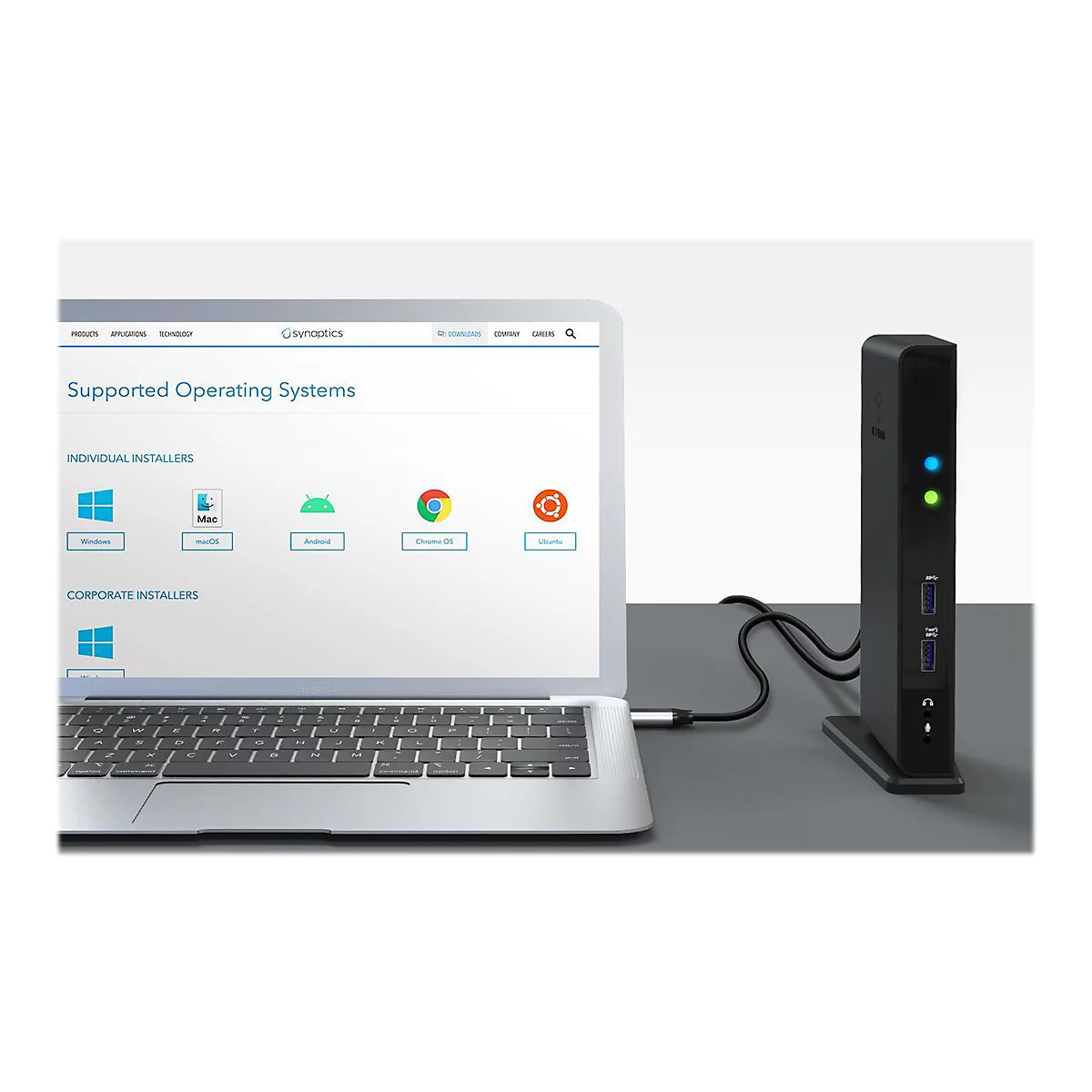 Laptop mit Dockingstation. Auf dem Bildschirm werden Betriebssysteme angezeigt. Die Dockingstation ist mit einem Kabel verbunden.