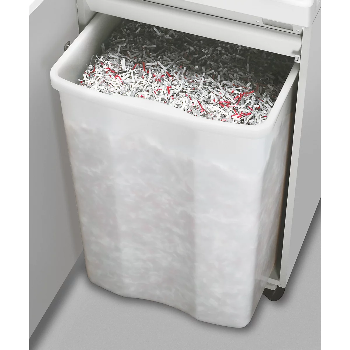 Der Abfallbehälter eines Aktenvernichters, gefüllt mit geschreddertem Papier, das teilweise rot gefärbt ist.