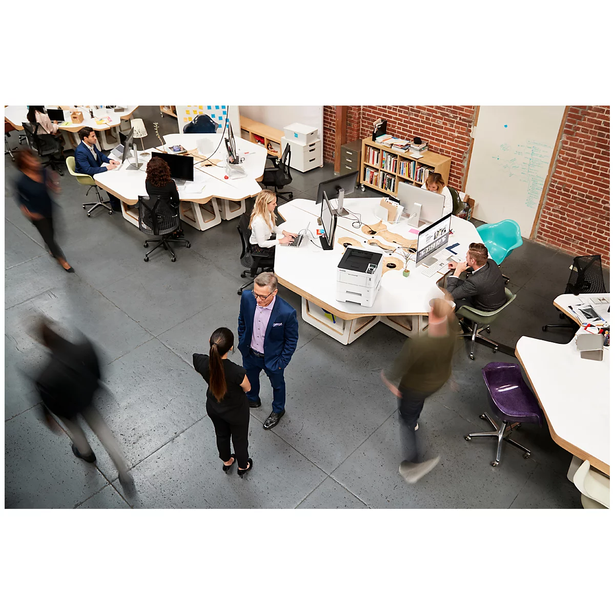 Vue aérienne d'une scène de bureau, plusieurs personnes travaillant et marchant autour de tables.