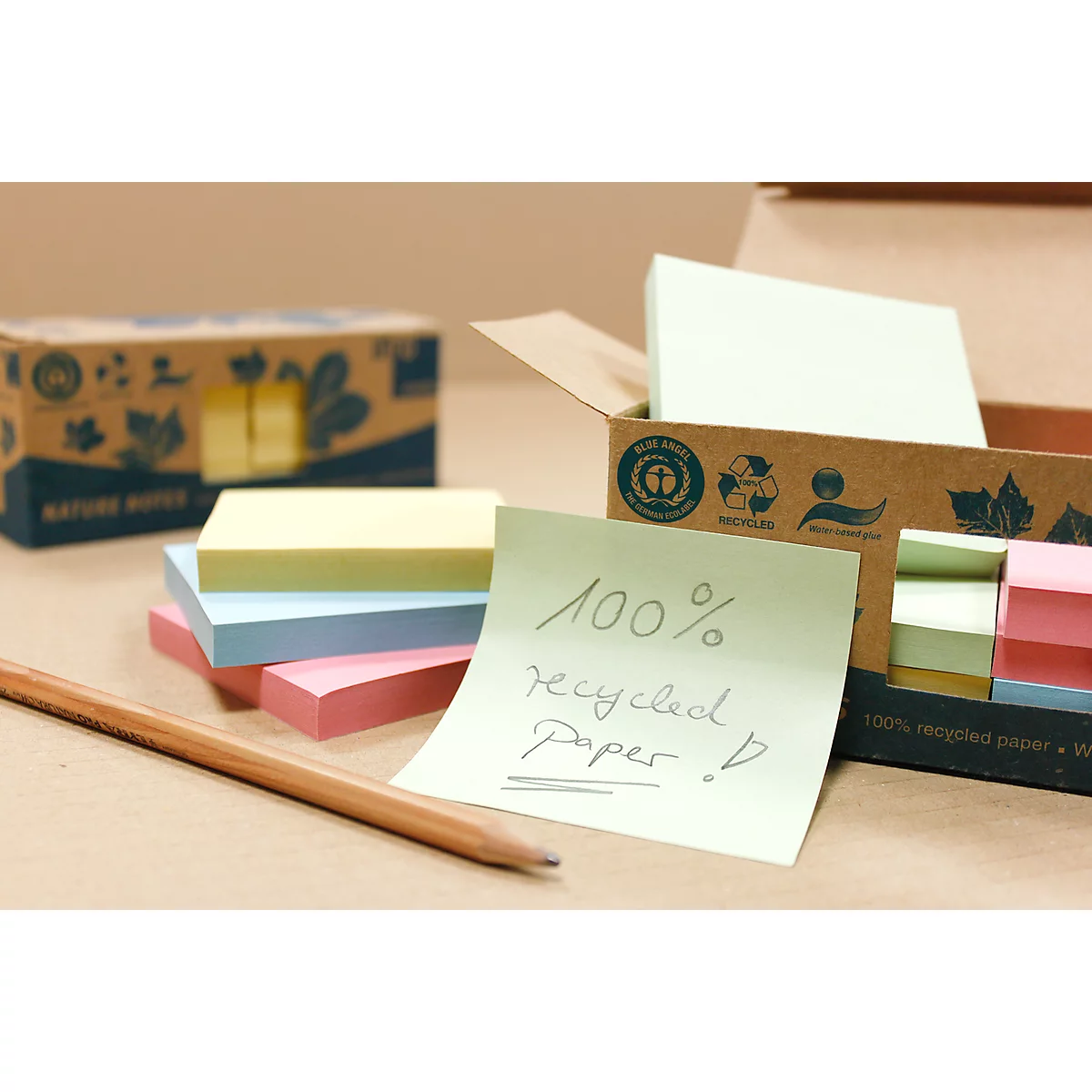 Post-it notes made from 100% recycled paper and a pencil, with more boxes of blocks in the background.