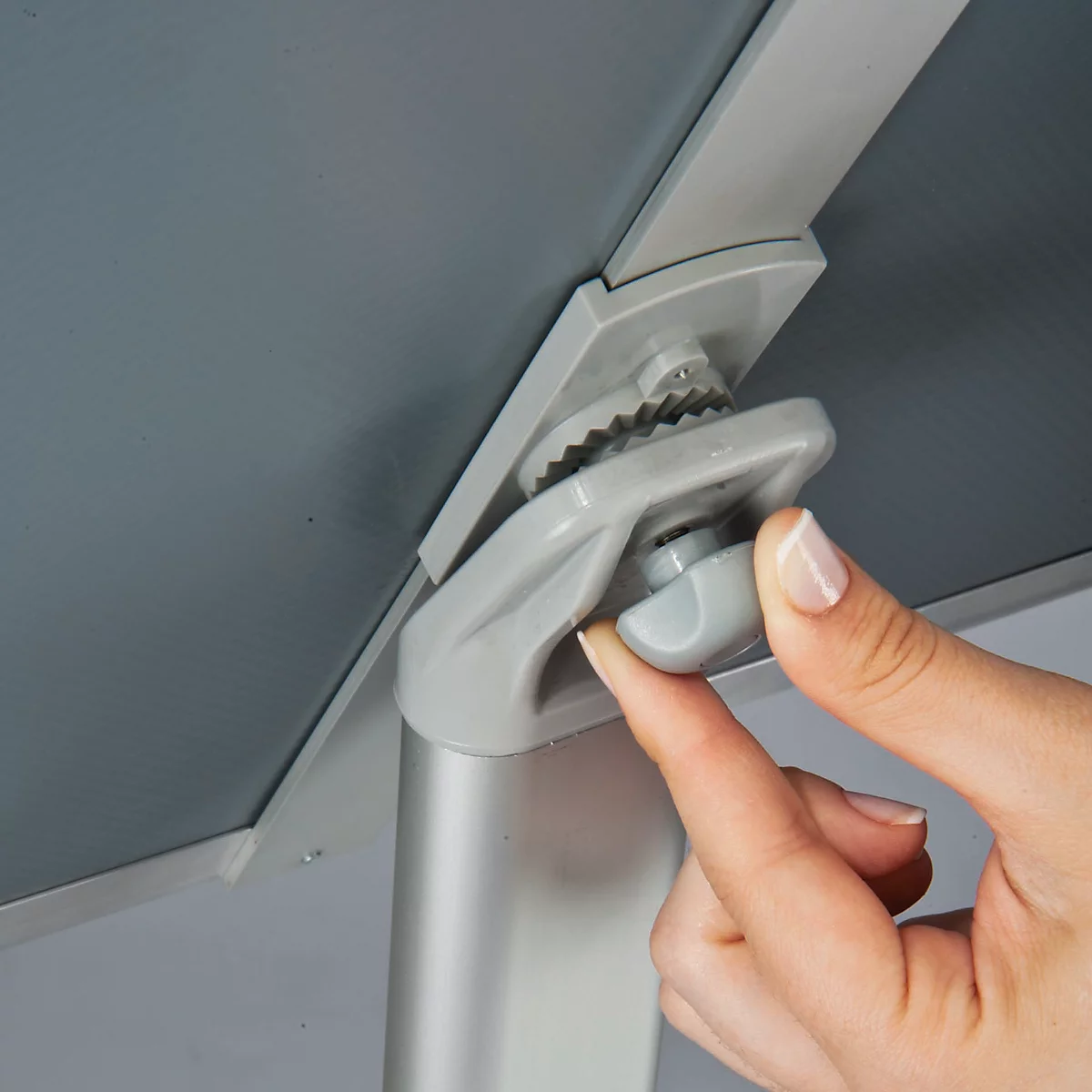 Close-up of a hand operating a grey twist closure to secure a grey panel to a metal rod.