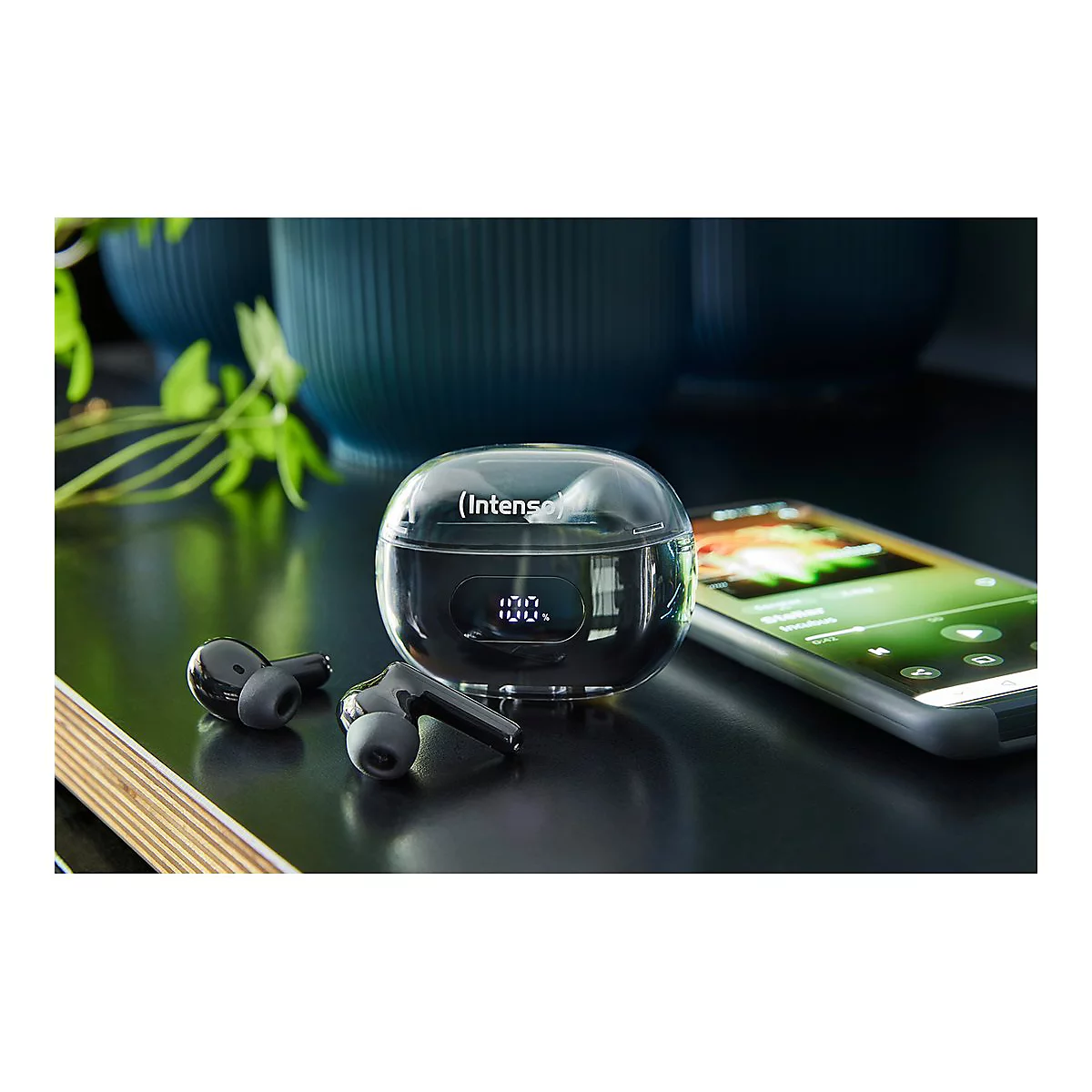 Schwarze Intenso True Wireless Kopfhörer mit Ladecase und Smartphone auf einem Tisch.
