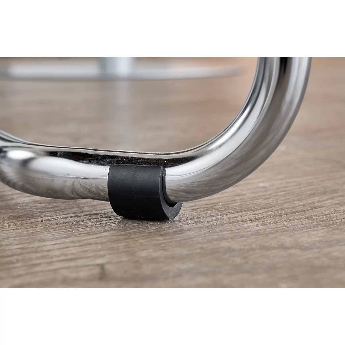 Close-up of a chrome chair leg with a black rubber protector on a wooden floor.
